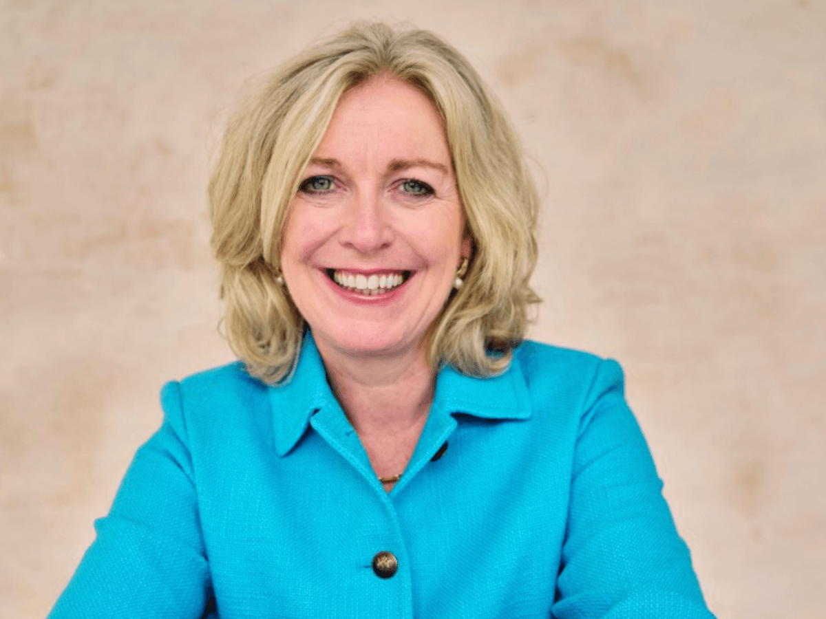 Een blanke vrouw van middelbare leeftijd met blond haar op schouderlengte in een helderblauw pak. 